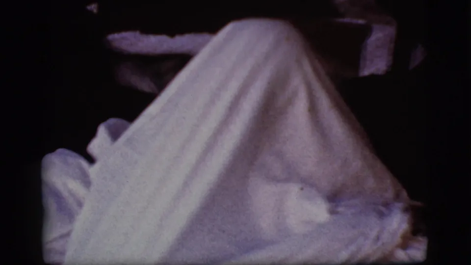 A white sheet forms a ghost-like silhouette in a dim 1968 Cottonwood, Arizona home-movie frame.