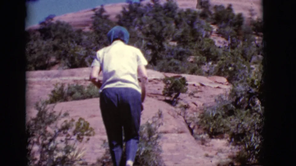The woman continues along the Arizona red rock path, framed from behind amid low shrubs and sunlit stone.