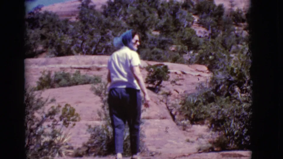 The hiker turns partly toward the camera while crossing red rock terrain in the Arizona desert setting.