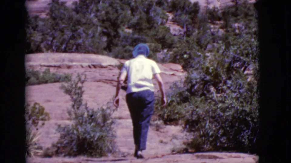 The woman moves away along a red rock trail bordered by desert plants in metadata-supported 1968 Arizona footage.