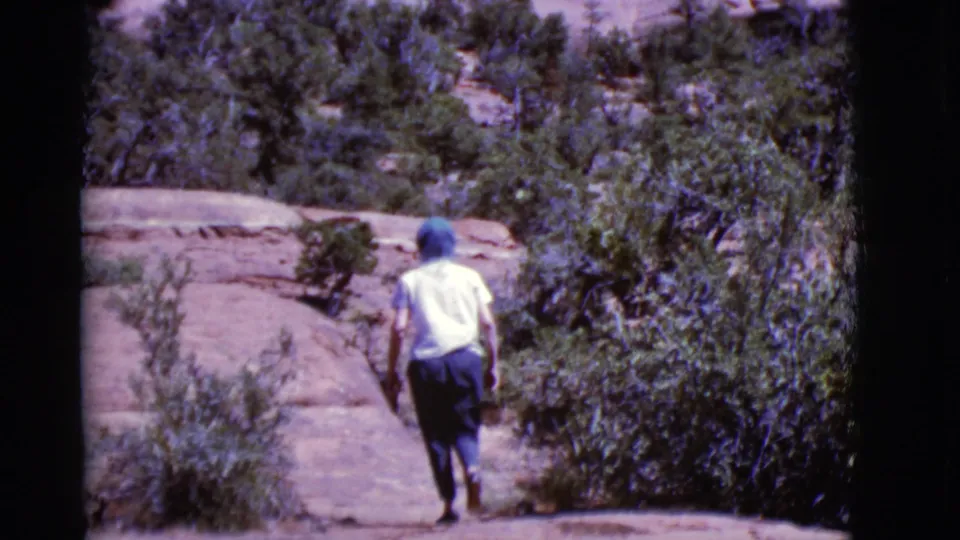 The hiker moves farther uphill through Arizona desert vegetation, filmed from behind on color 8mm stock in 1968.
