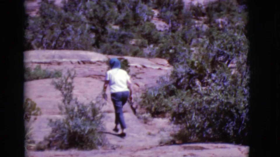A rear-view 1968 Arizona hiking shot shows the person crossing uneven sunlit rock with scrub vegetation close to the path.