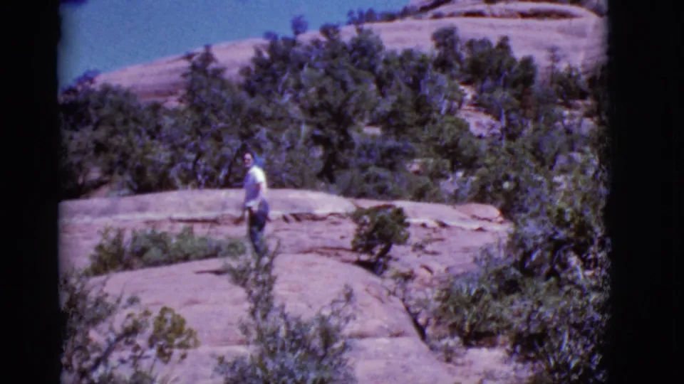 The woman pauses near the top of the Arizona rock trail, turning back toward the home-movie camera.