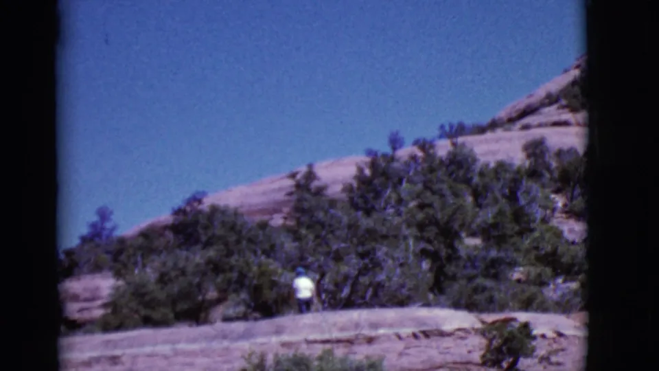 The final frame keeps the man small in the landscape, walking through a rocky Arizona desert setting with scrub and sandstone.
