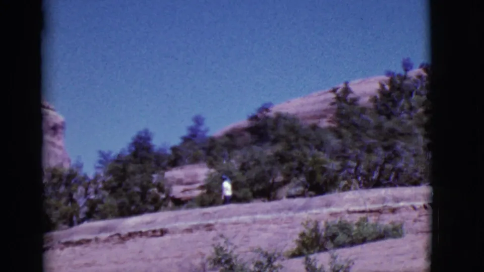 A lone person in white remains visible near brush and trees on a rocky Arizona slope in the final frame.