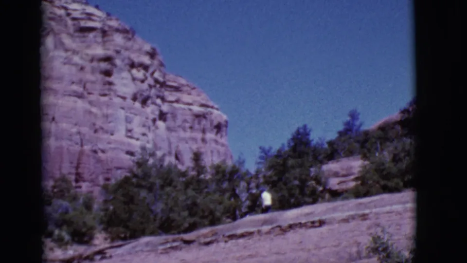 1968 Arizona 8mm frame emphasizing red sandstone cliffs and trees, with the walker near the lower right edge.