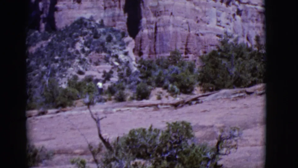 Arizona 1968 frame with scrub-covered sandstone terrain below a vertical red rock formation.