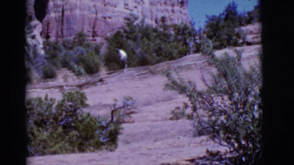 Arizona 1968 frame showing a man walking through scrubby sandstone terrain beneath red rock formations.