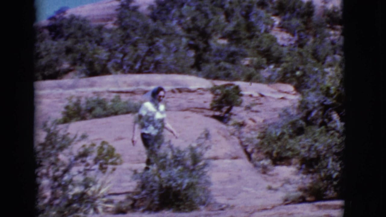 Woman walks across pale rock slabs bordered by desert shrubs.