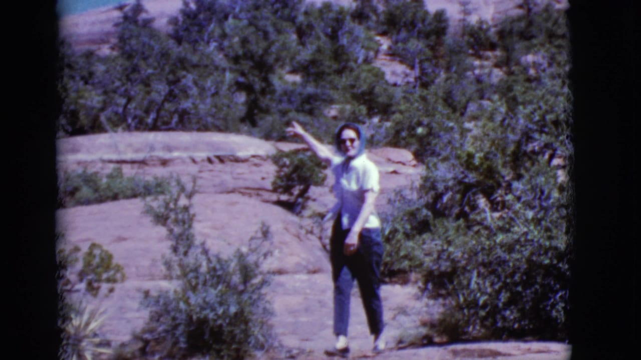 Woman in sunglasses and headscarf points while standing on a rocky desert trail.