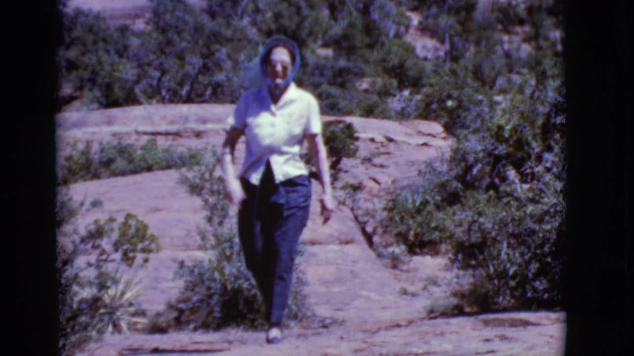 Woman walks toward the camera on a rocky trail bordered by desert shrubs.