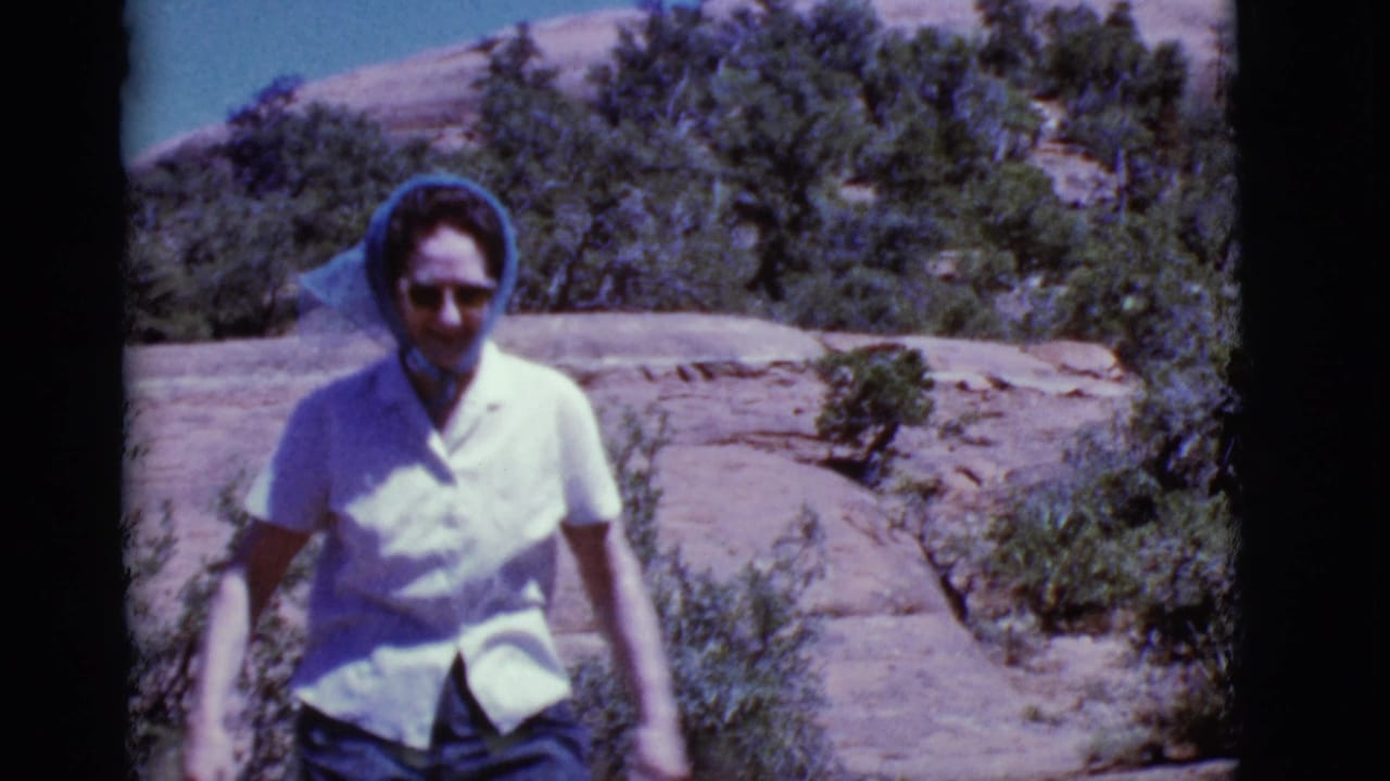 Woman in sunglasses and a blue headscarf walking down a rocky desert hillside.