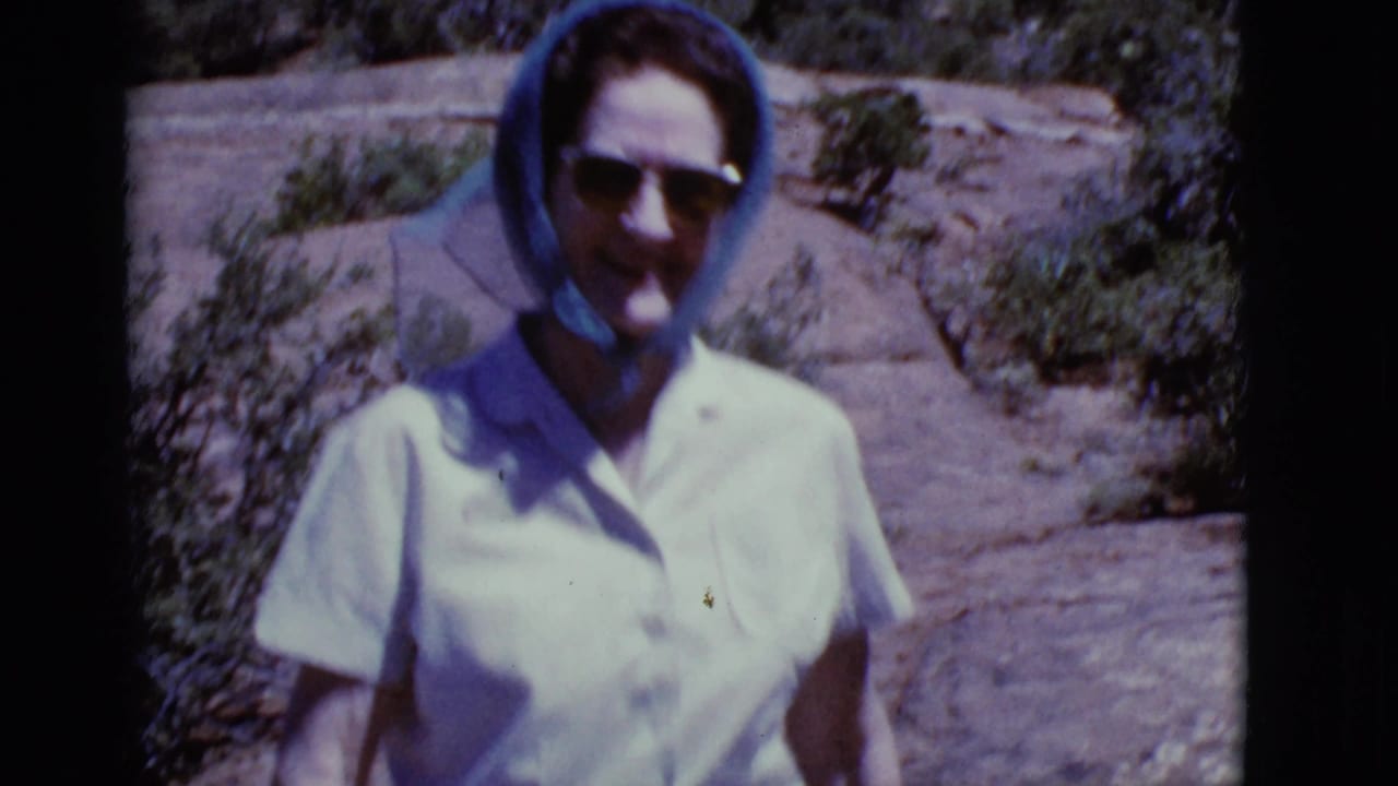 Closer view of the woman standing on rocky ground with shrubs behind her.
