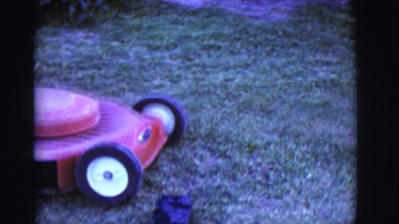Red push lawnmower on grass with part of a wheel and mower body visible.