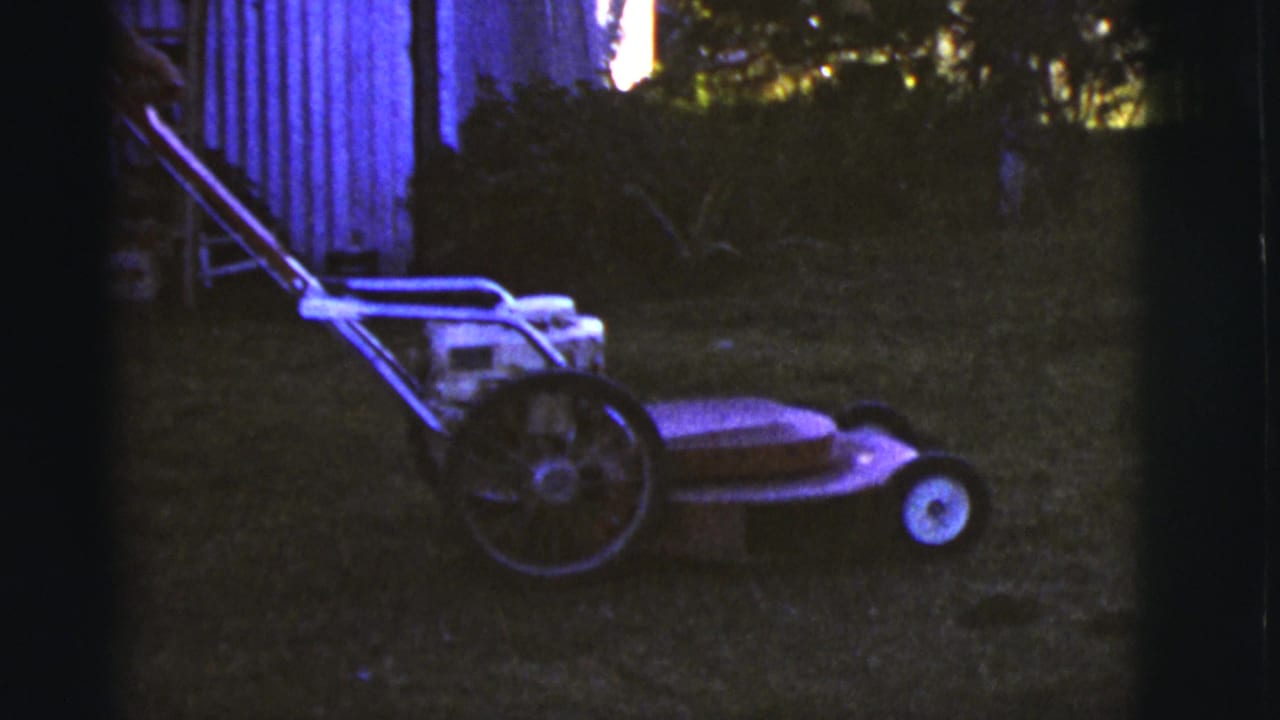Push lawnmower on grass beside a wooden shed in a dim yard.