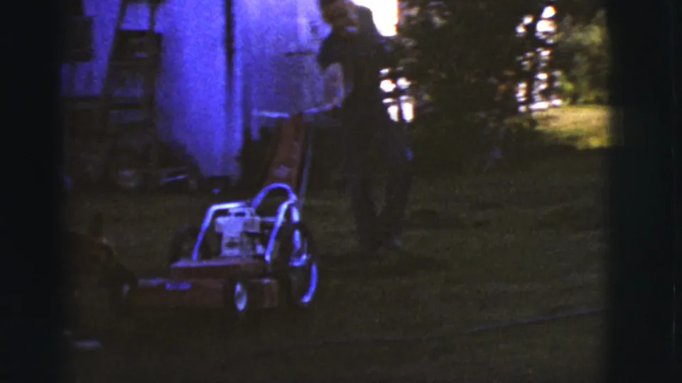 1968 Arizona 8mm frame showing a German Shepherd near a push lawnmower while an adult man stands in the yard beside a shed.
