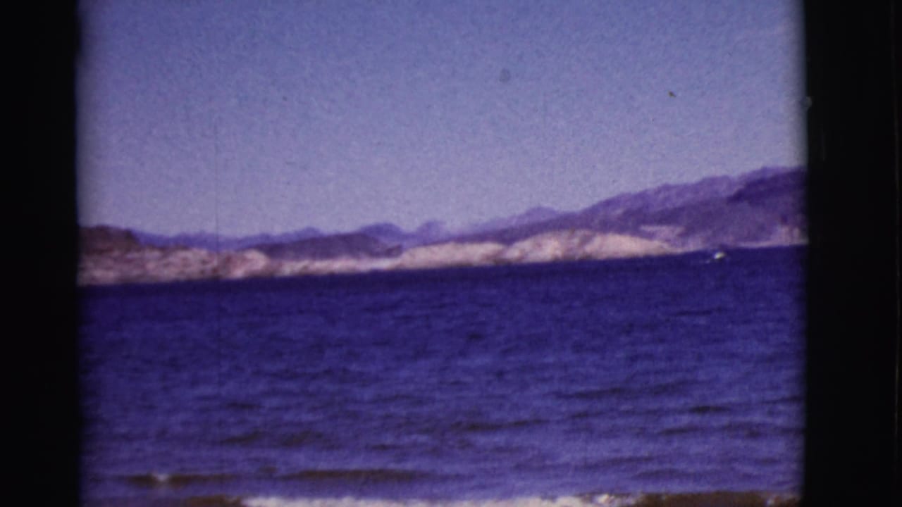 Blue lake water with distant arid mountains and a small boat near the shoreline.