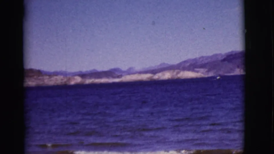 1968 Arizona home-movie view of blue lake water, distant mountain ridges, and a tiny boat near the pale shore.