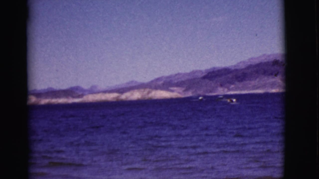1968 Arizona lake scene with small distant boats crossing blue water below rugged mountain slopes.
