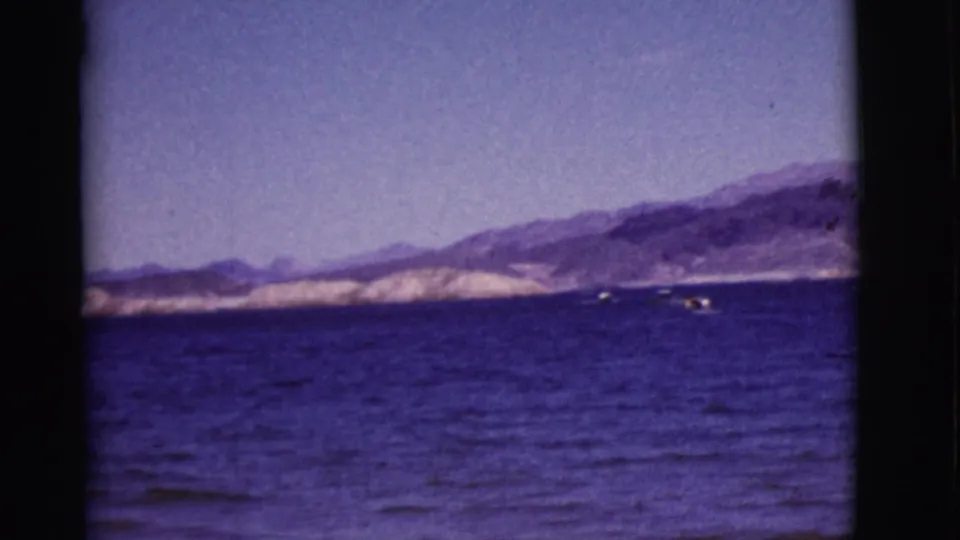 1968 Arizona lake scene with small distant boats crossing blue water below rugged mountain slopes.