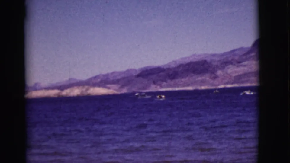 Vintage 8mm view of an Arizona lake, with small boats spread across blue water below arid mountain terrain.