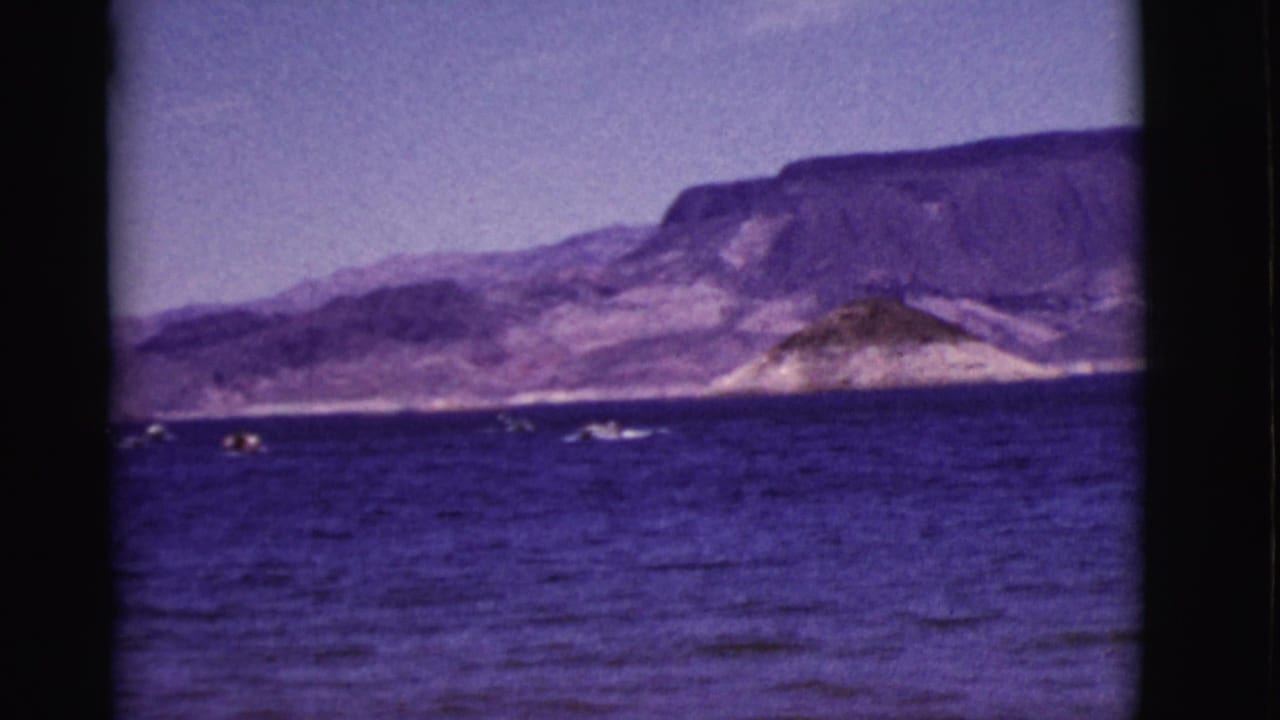 Purple-blue water with small boats and distant rugged mountains under a hazy sky.
