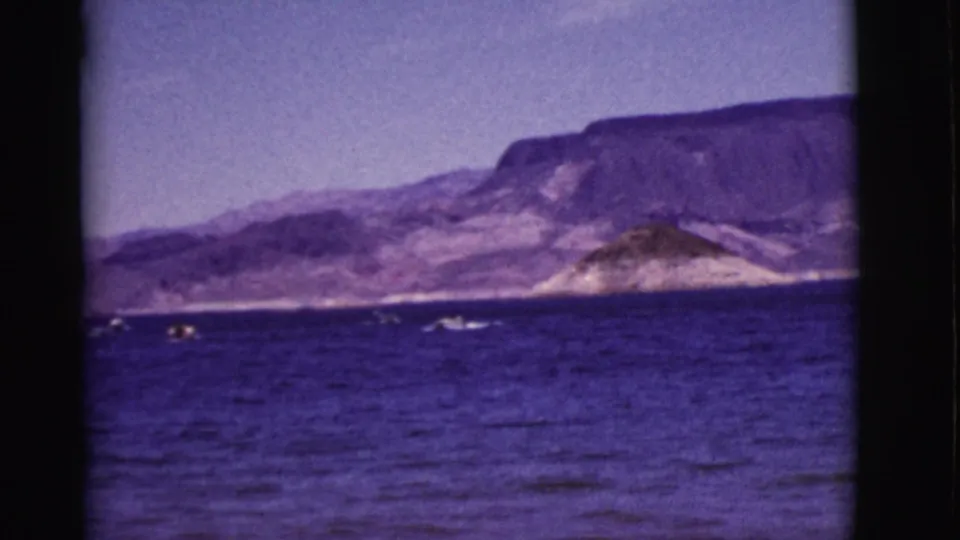 1968 Arizona 8mm frame showing small boats on purple-blue water with a distant mountain shoreline and hazy sky.