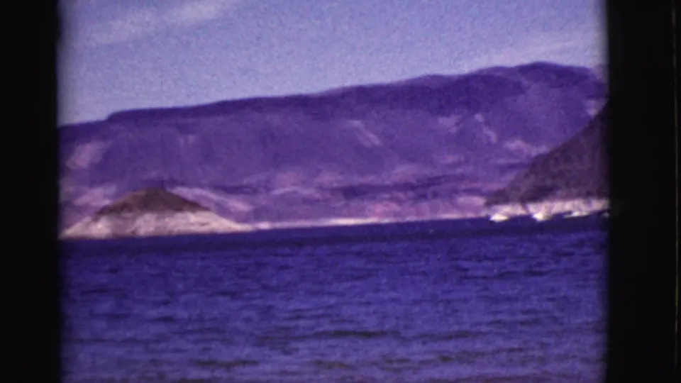 1968 Arizona home-movie frame with purple-blue water, distant shoreline, and small white boats near mountain slopes.
