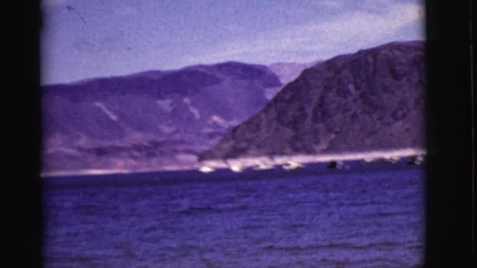 1968 Arizona 8mm frame showing blue water, small boats, a bright far shore, and a large dark mountain slope.