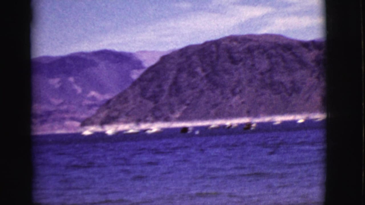 Small boats on a blue lake below rugged mountains and a pale sky.