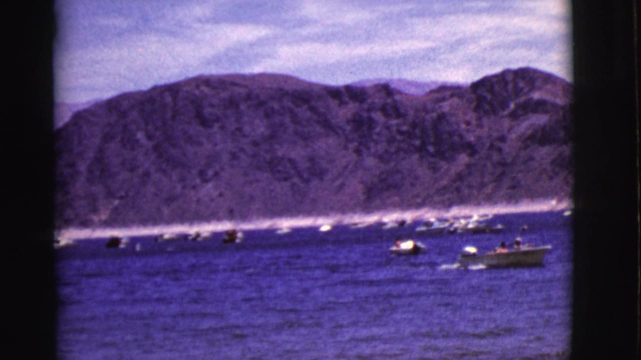 Motorboats and sailboats scattered across a lake in front of rocky hills.