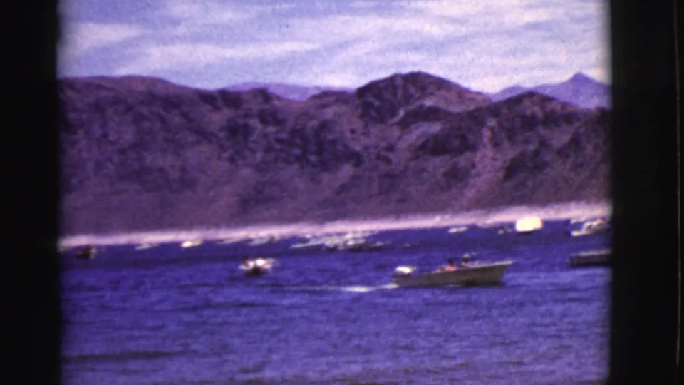 Vintage 8mm view of multiple small boats crossing a blue Arizona lake beneath dry mountain ridges.