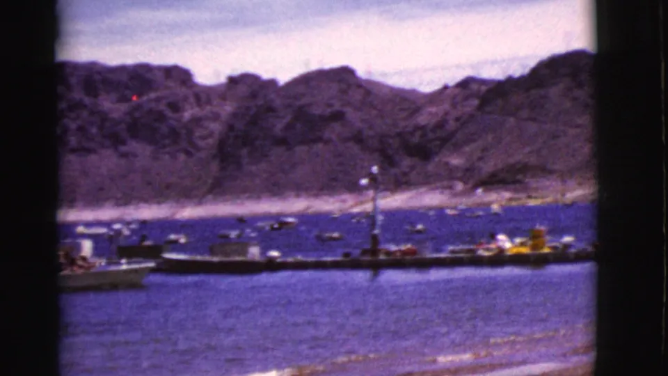 1968 Arizona lake scene with a long dock, small boats, distant people, and rugged arid cliffs captured on 8mm film.