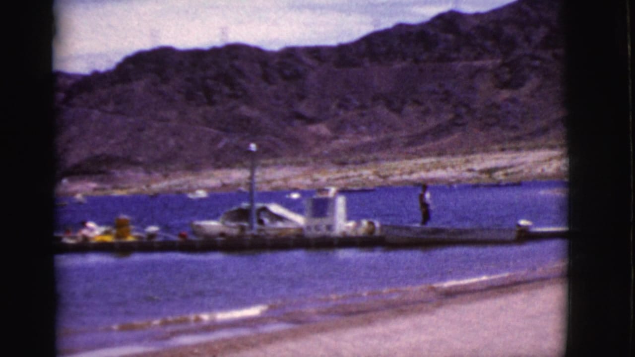 Person walking on a dock beside a lake with mountains behind.