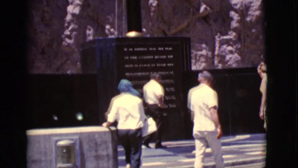 Visitors at an outdoor memorial site in Arizona stand near a dark inscribed stone monument set against rocky terrain.