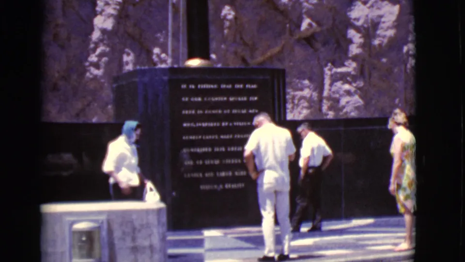 1968 Arizona frame of visitors standing near an inscribed memorial panel, with bright sun and soft 8mm color.