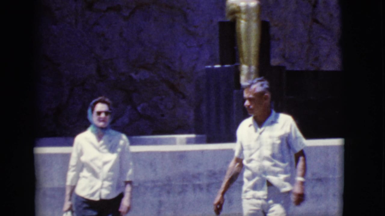 Older couple walking near a dark wall with a gold-toned statue behind them.