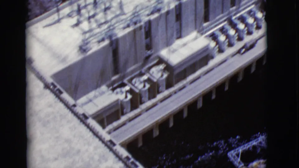 Home-movie frame looking down at a sunlit architectural edge with columns, shadows, and water or dark ground below.