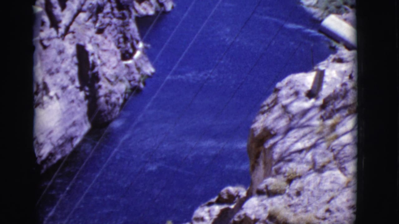 1968 Arizona home-movie view looking down over a blue canyon river, rugged cliffs, and power lines spanning the water.