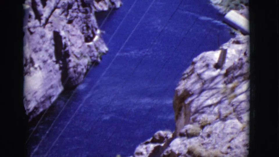 1968 Arizona home-movie view looking down over a blue canyon river, rugged cliffs, and power lines spanning the water.
