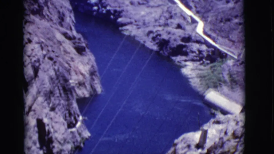 Arizona canyon view with blue river water, steep rock walls, power lines, and a pale route or structure near the canyon edge.