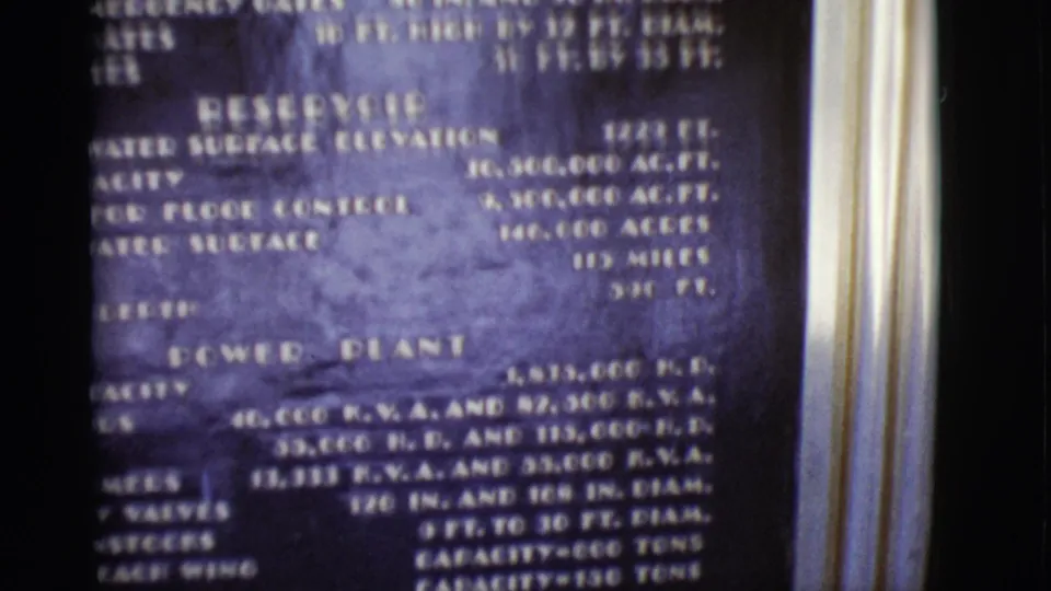 1968 Arizona 8mm frame of the lower dam information board, showing reservoir and power plant specification text.