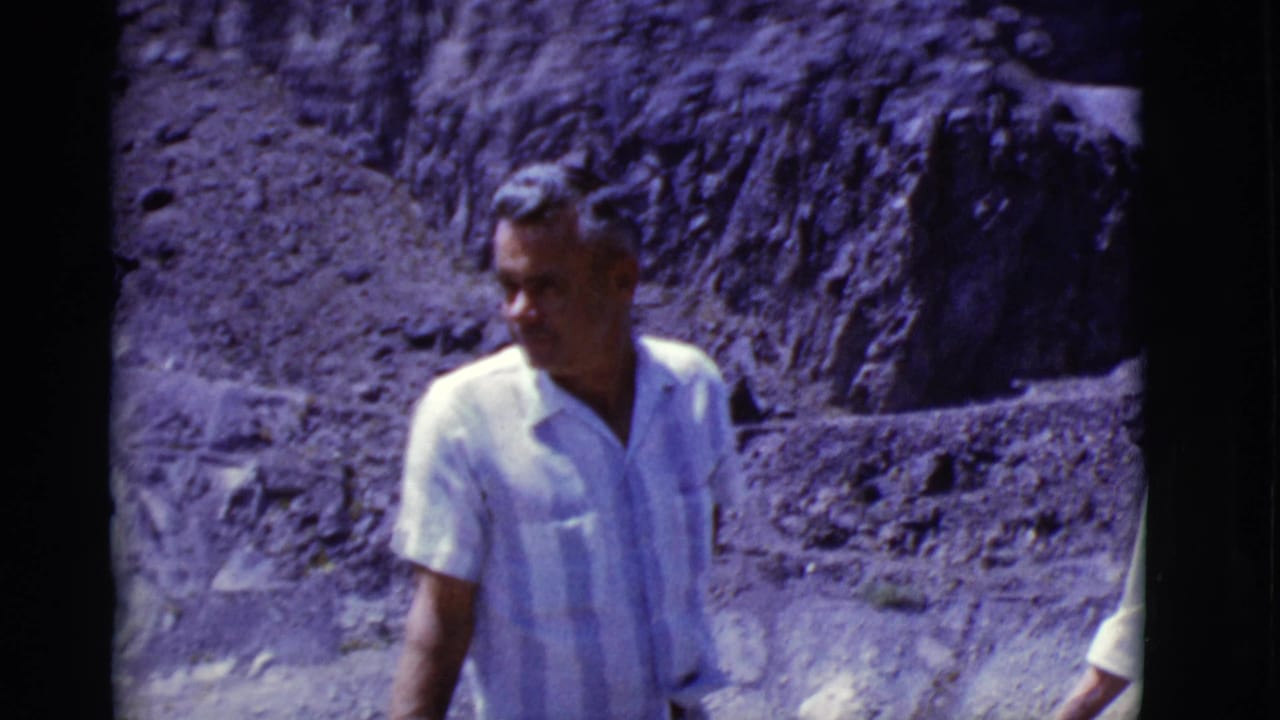 A man in a light short-sleeve striped shirt moves through the frame against rocky Arizona desert terrain in 1968 home-movie footage.