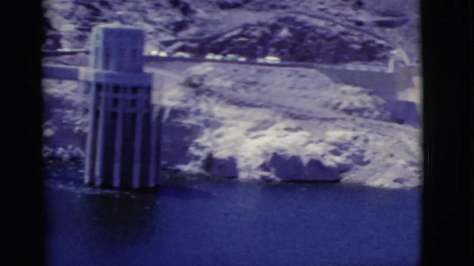 Hoover Dam intake tower stands in Lake Mead, backed by pale rocky desert terrain and a dam roadway.
