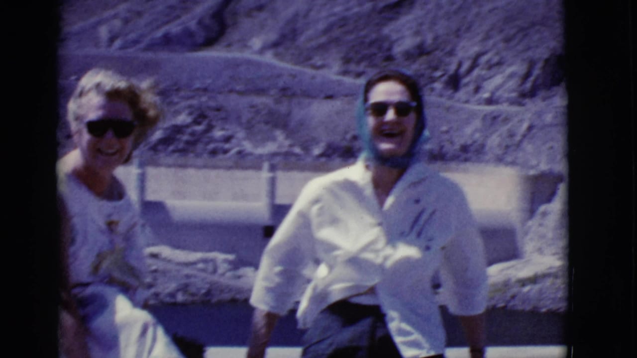 1968 Arizona home-movie frame showing two adults smiling outdoors, one in a light shirt and headscarf.