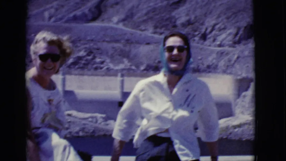 1968 Arizona home-movie frame showing two adults smiling outdoors, one in a light shirt and headscarf.