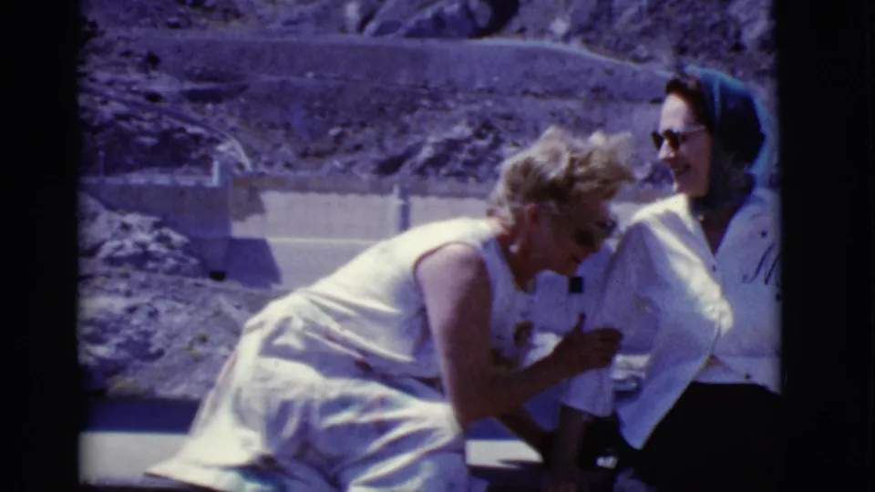 1968 Arizona home-movie frame of a woman leaning toward a man in a headscarf as they laugh outdoors.