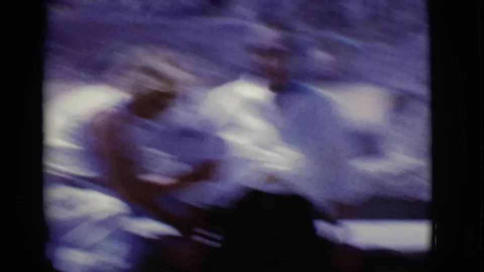 Blurred 1968 Arizona home-movie frame showing two women seated at a desert dam site in bright summer clothing.