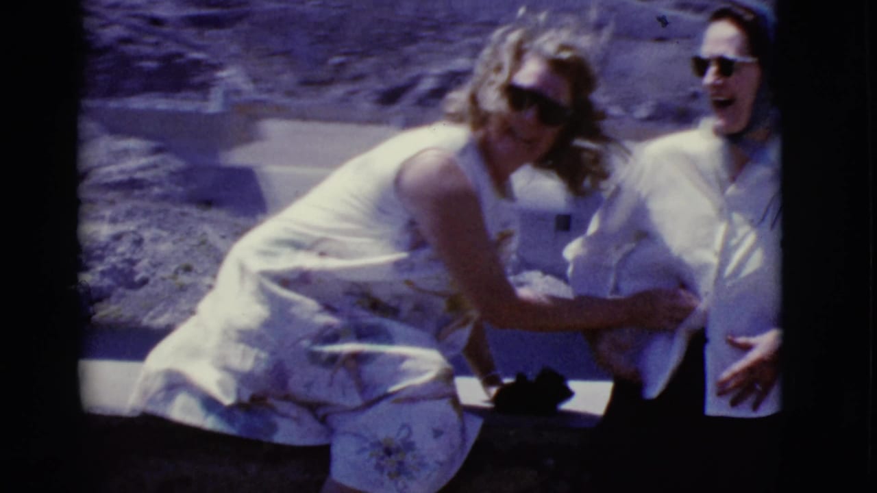 Two adult women in sunglasses laugh and lean together at an Arizona desert dam site in 1968 home-movie footage.
