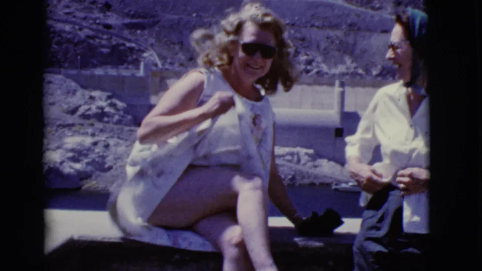 A smiling woman in sunglasses sits near another woman at a 1968 Arizona desert dam location.